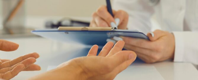 Two people in discussion; one holds out hands while the other writes on a clipboard, possibly related to grant writing.