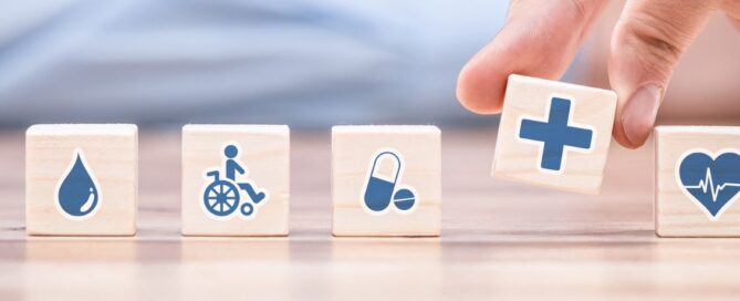 Hand arranging wooden blocks with healthcare icons: blood drop, wheelchair, pills, medical cross, and heartbeat. Concept of grant writing in healthcar