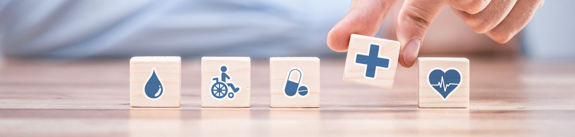 Hand arranging wooden blocks with healthcare icons: blood drop, wheelchair, pills, medical cross, and heartbeat. Concept of grant writing in healthcar