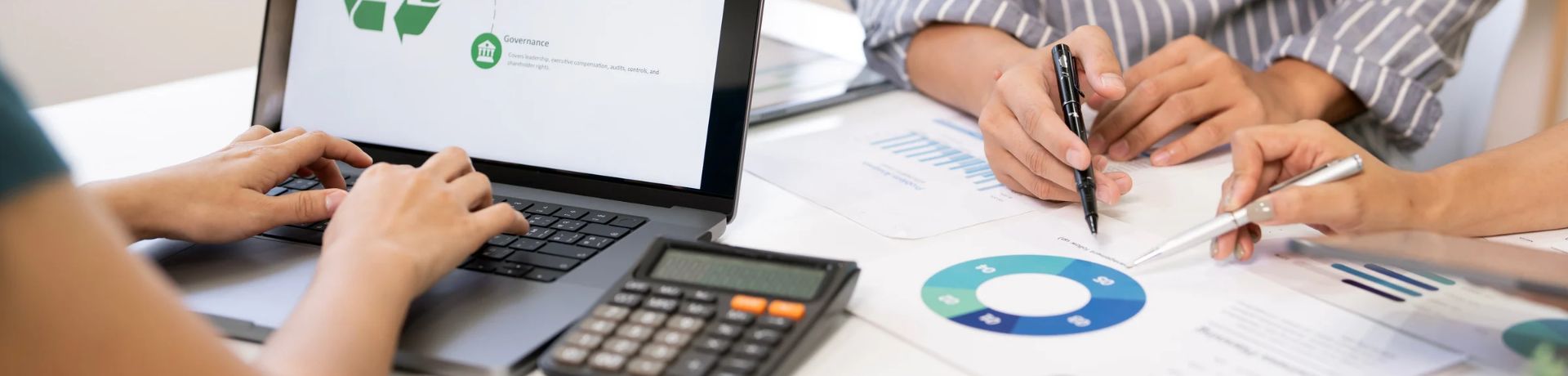 Hands typing on a laptop with data charts and a calculator nearby, suggesting teamwork in grant writing and financial planning.